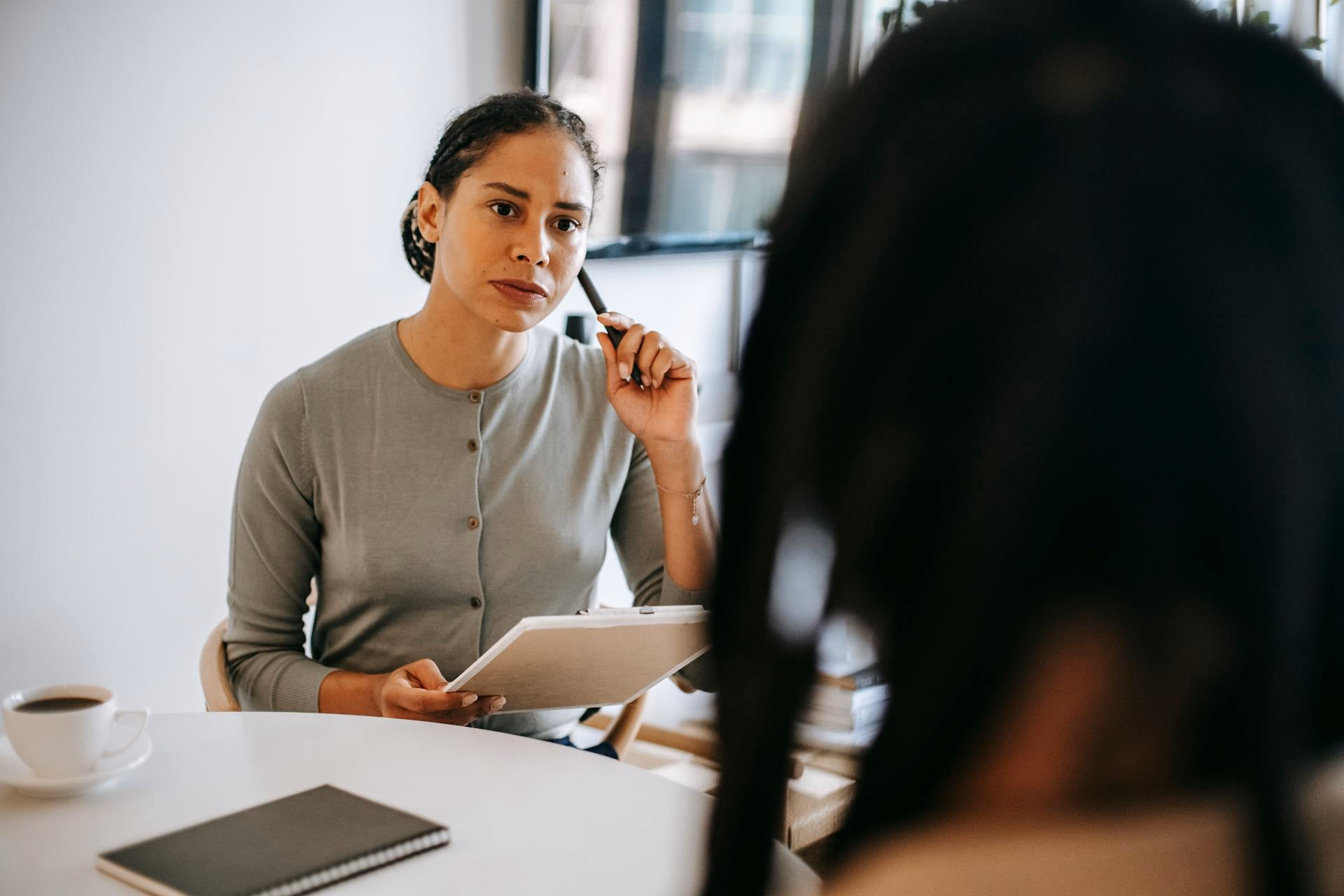 Clinician in a gray sweater holding a pen and clipboard during a patient conversation