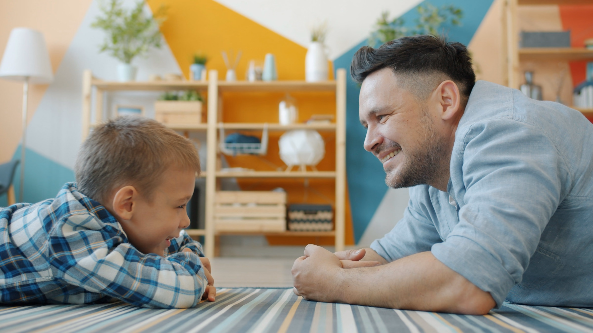 Father and young son lying on a striped rug, smiling as they talk