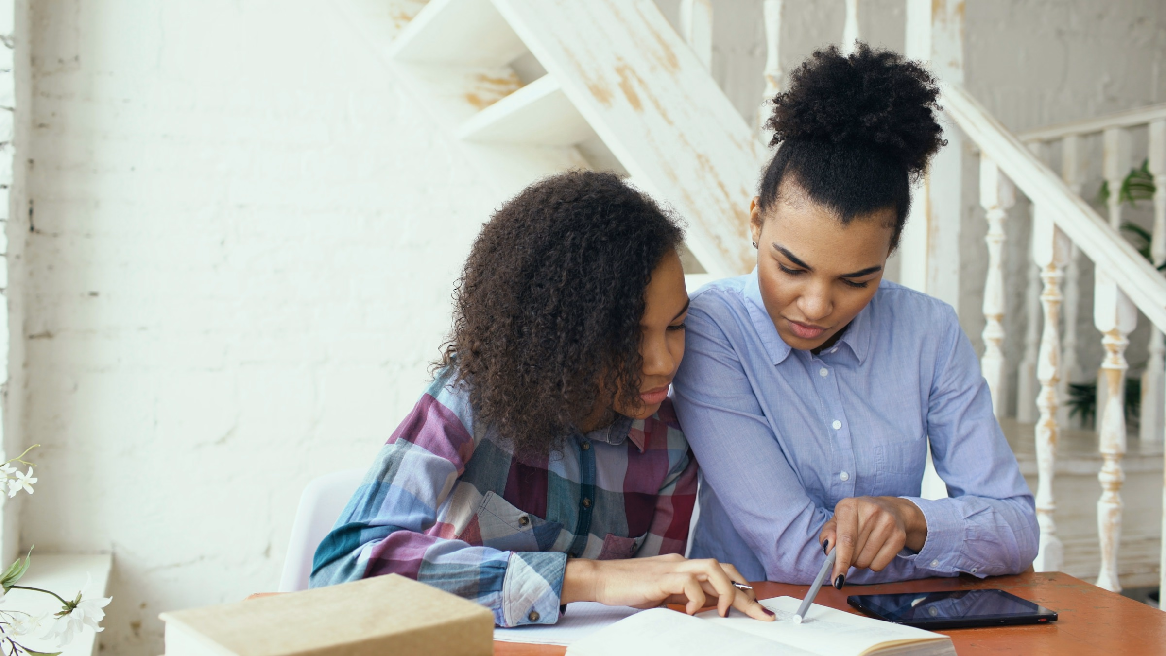 Mother helping her teenage daughter with schoolwork at a table