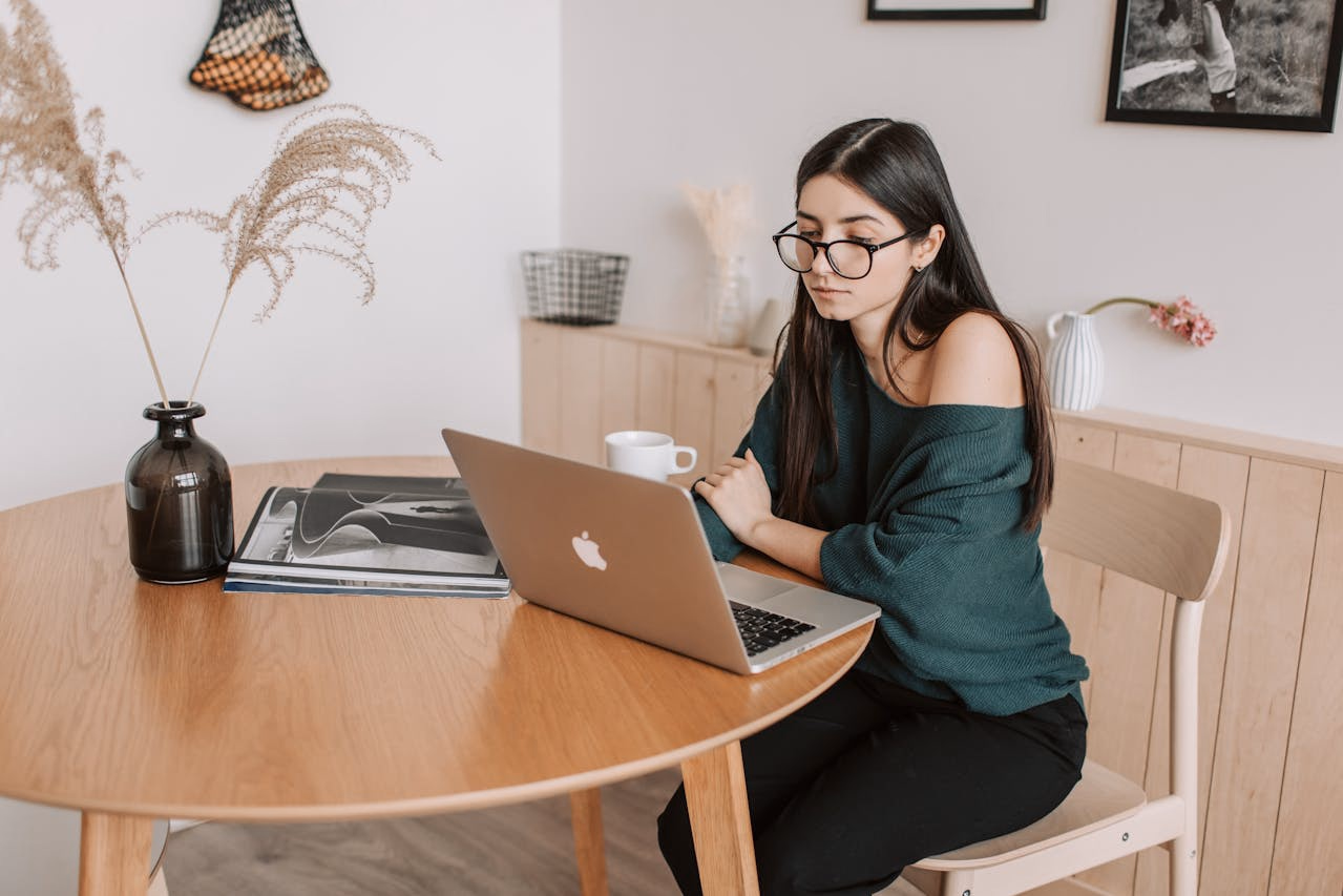 Woman in glasses at a wooden table attending an online psychiatry visit on a laptop